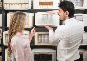 The young salesman tells the customer about quality mattresses in the store.
