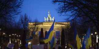 Demonstrierende mit Ukraineflaggen und Schildern, im Hintergrund das erleuchtete Brandenburger Tor. Bild: IMAGO / Achille Abboud