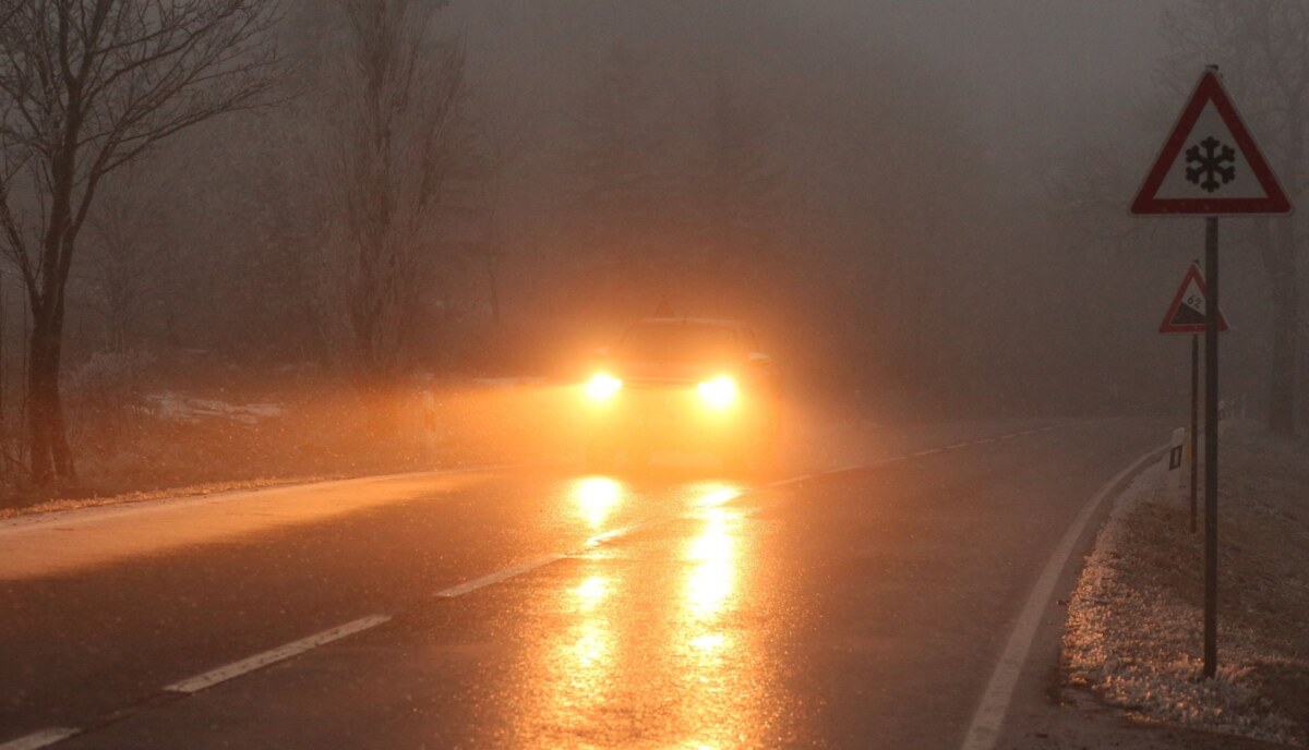 Ein Auto fährt bei Glatteis und Nebel über eine Straße.