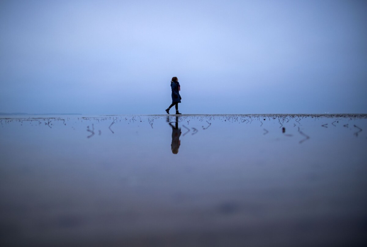 Eine Frau geht über eine Sandbank an der Ostseeküste.