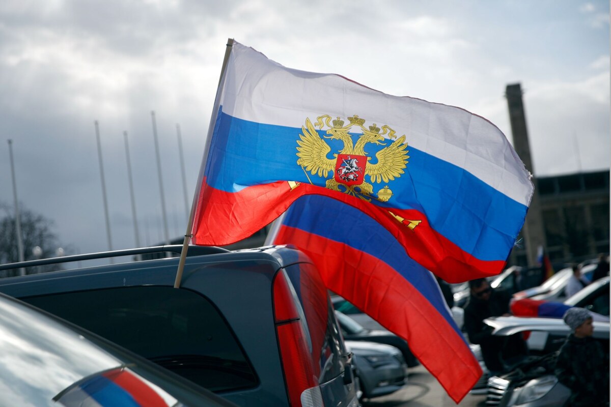 Flaggen mit den russischen Nationalfarben und dem russischen Staatswappen wehen an einem Auto.