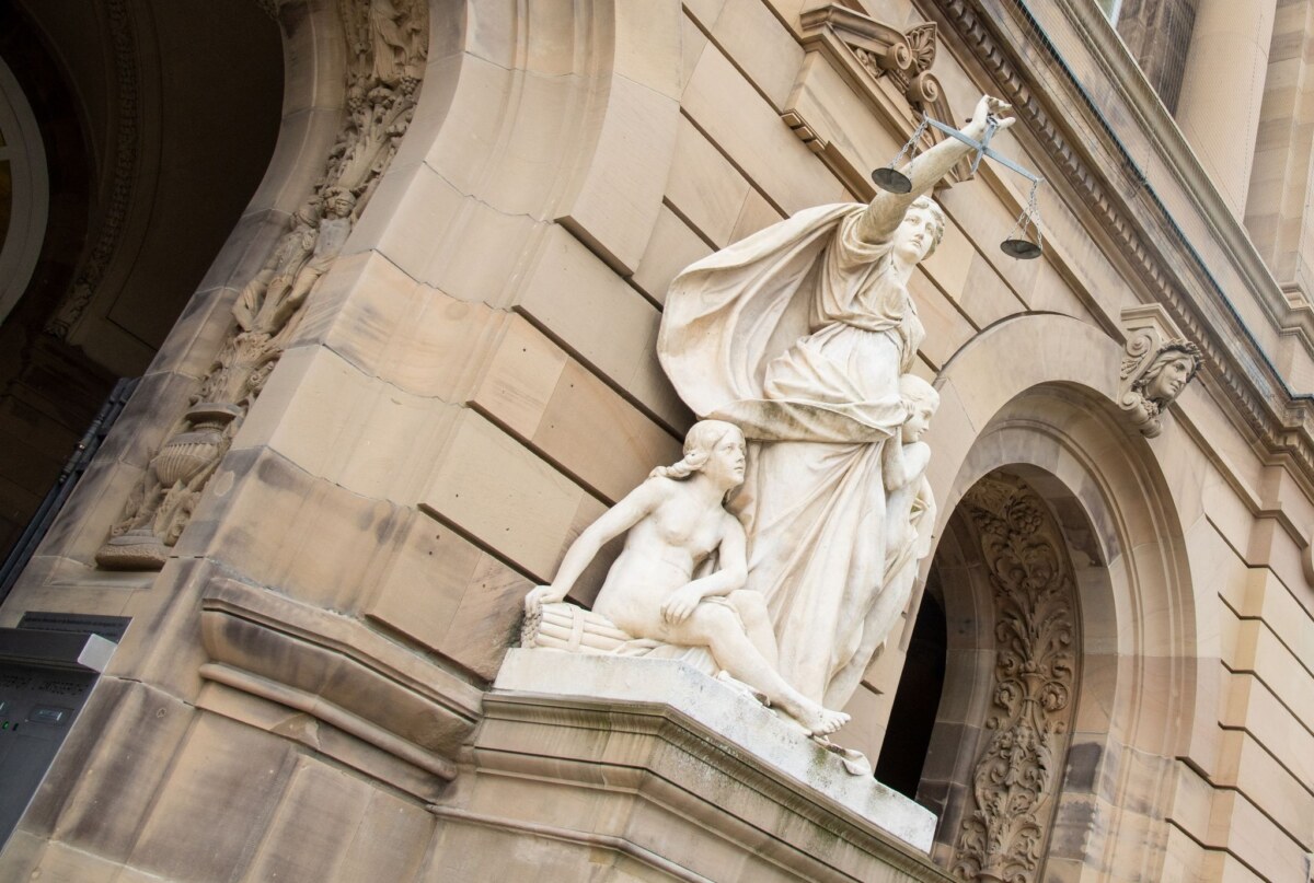 Vor einem Landgericht hält eine Statue der Justitia eine Waagschale.