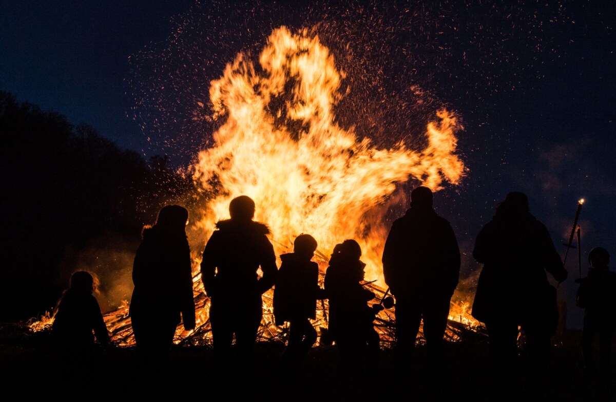 Menschen stehen an einem traditionellen Osterfeuer. An Osterfeuern haben viele Menschen Freude.