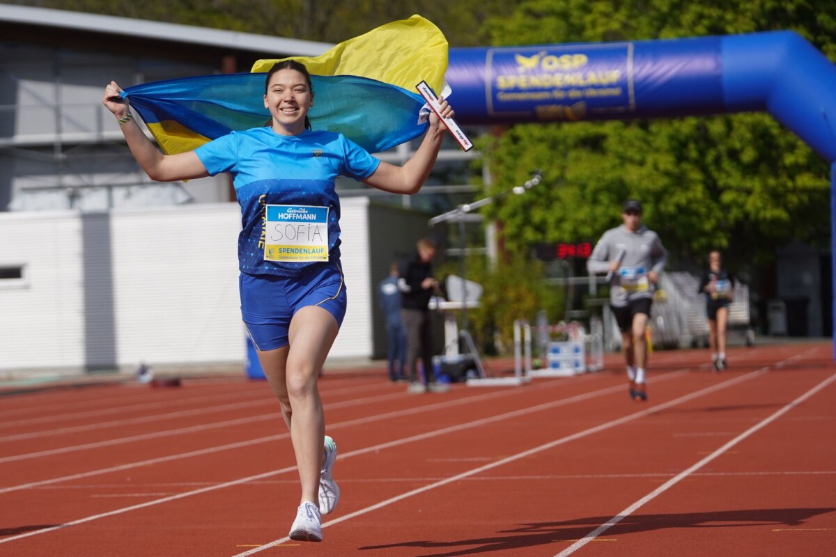 Die Läuferin Sofia läuft mit einer ukrainischen Flagge am Spendlauf für geflüchtete ukrainische Sportler und Sportlerinnen.