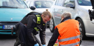 Klimaschützer haben sich auf der Straße festgeklebt. Ein Polizist versucht, die festgeklebten Hände mit Speiseöl von der Straße zu lösen.