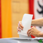 Jemand steckt einen Umschlag in eine Wahlurne.