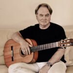 Klaus Hoffmann sitzt mit seiner Gitarre auf dem Sofa.