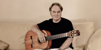 Klaus Hoffmann sitzt mit seiner Gitarre auf dem Sofa.