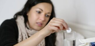 Junge Frau wirft sich eine Aspirin-Tablette in ein Glas Wasse.