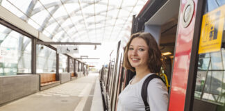 Junge Frau steht lächelnd auf dem Bahnsteig.