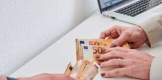 Eine Männerhand hält ein Bündel 50-Euro-Scheine, während eine Frauenhand nur wenige 50-Euro-Scheine hält.