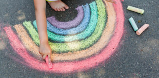 Kind malt Regenbogen auf Straße.