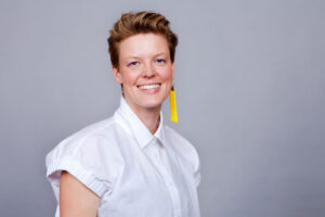 Katalin Gennburg in weißer Bluse mit kurzen Ärmeln, kurze bräunliche Haare, gelber Ohranhänger, lächelt