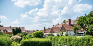Häuser mit Giebeln aus Holz und Ziegeln auf dem Dach stehen hinter grünen Hecken und Bäumen: Gartenstadt Staaken
