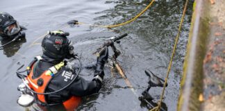 Zwei Taucher der DLRG heben ein altes Fahrrad aus dem Wasser.