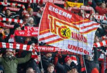 Fans von Union Berlin feuern ihr Team mit Schals und Fahnen an.