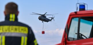 Ein Hubschrauber der Luftwaffe fliegt mit einem Wasserbehälter während einer Übung in Müncheberg.