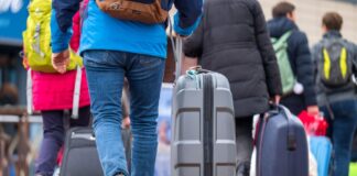 Touristen laufen mit Rollkoffern am Bahnhof entlang.