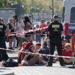Polizeibeamte stehen um eine Gruppe festgesetzter Mitglieder der Klimaschutzgruppe Letzte Generation.
