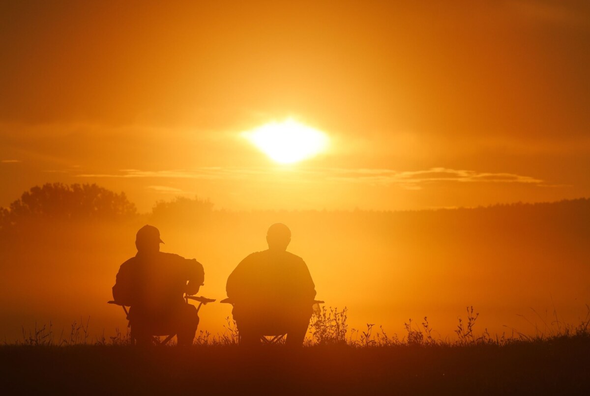 Fischwilderei Zwei Angler sitzen auf Campingstühlen und schauen sich den Sonnenaufgang an.