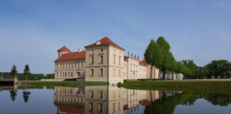 Die Parkseite von Schloss Rheinsberg mit dem Kurt Tucholsky Literaturmuseum spiegelt sich im Wasser.