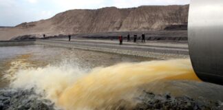 Aus einem Flutungsrohr strömt Wasser in einen ehemaligen Tagebau.