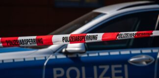 Ein Polizeiauto steht hinter einem Absperrband der Polizei.