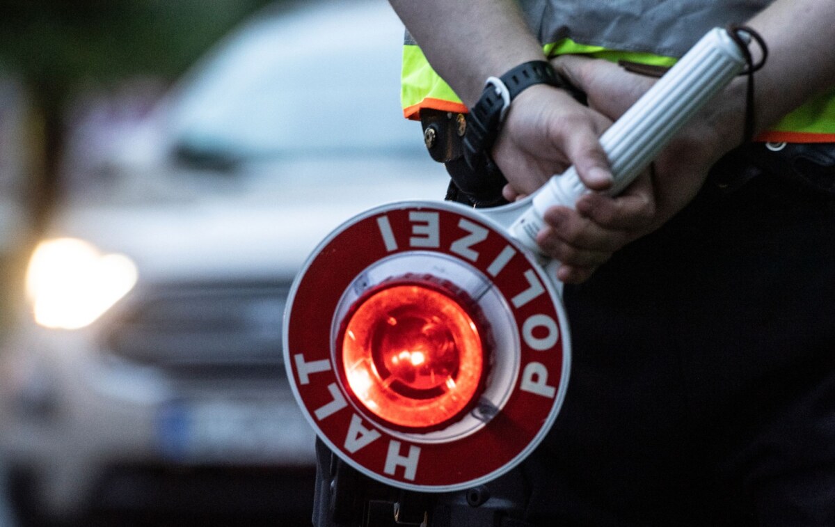 Polizeikontrolle Ein Polizist hält bei einer Verkehrskontrolle eine Winkerkelle in der Hand.