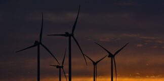 Farbenprächtig leuchten am frühen Morgen die Wolken im Sonnenaufgang über der Landschaft mit mehreren Windrädern.