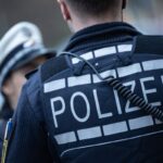 Eine Polizistin (l) und ein Polizist stehen an einer Straße.