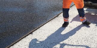 Der Schatten eines Bauarbeiters fällt auf den Boden einer Straße, die asphaltiert wird.