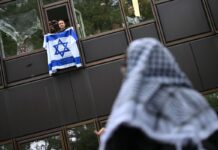 Eine Frau hält während einer propalästinensischen Demonstration der Gruppe «Student Coalition Berlin» auf dem Theaterhof der Freien Universität Berlin vor Unterstützern außerhalb des Camps eine Israelflagge aus einem Fenster.