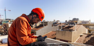 Ein Arbeiter installiert Solarmodule auf einem Hausdach. Foto: IMAGO / Westend61