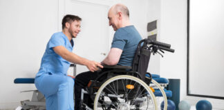 Ein männlicher Pflegeassistent hilft einem Mann im Rollstuhl. Foto: IMAGO / Zoonar