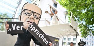 Ein Aktivist mit Merz-Maske zerbricht während einer symbolischen Protestaktion von Kabul Luftbrücke und Campact ein Schild mit der Aufschrift «Versprechen». 