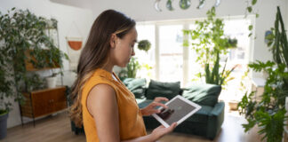 Eine Frau steuert per Tablet ihr Smart Home. Foto: IMAGO / Westend61