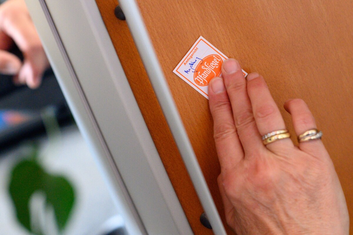 Gerichtsvollzieher Eine Gerichtsvollzieherin klebt ein Pfandsiegel auf ein technisches Gerät. (Symbolbild)