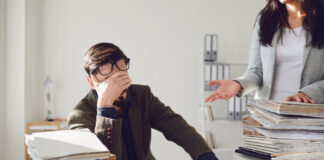 Fachkräftemangel in Berlin erhöht den Druck auf Unternehmen Ein gestresster Mitarbeiter sitzt vor einem Stapel Akten mit Lohnabrechnungen. Bild: iStock / Getty Images Plus / Lacheev