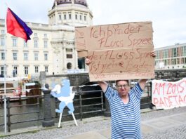 Schwimm-Demo an der Spree fällt ins Wasser Ein Mann steht während der Schwimm-Demonstration gegen das Badeverbot in der Spree mit einem Schild am Ufer.
