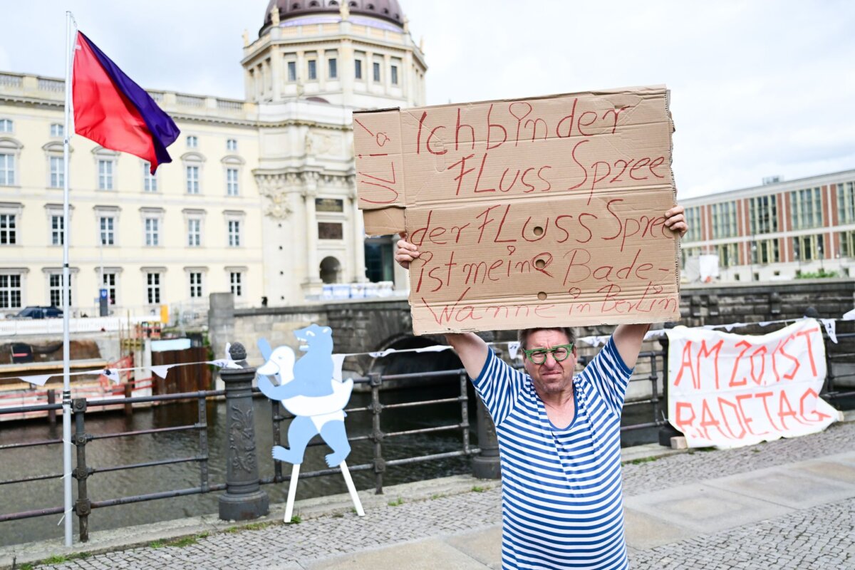 Schwimm-Demo "101 Jahre Badeverbot abwählen!" Ein Mann steht während der Schwimm-Demonstration gegen das Badeverbot in der Spree mit einem Schild am Ufer.